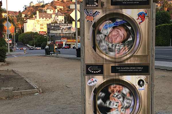 Un artista callejero muestra en un cartel a Leonardo DiCaprio y Hillary Clinton lavando dinero
